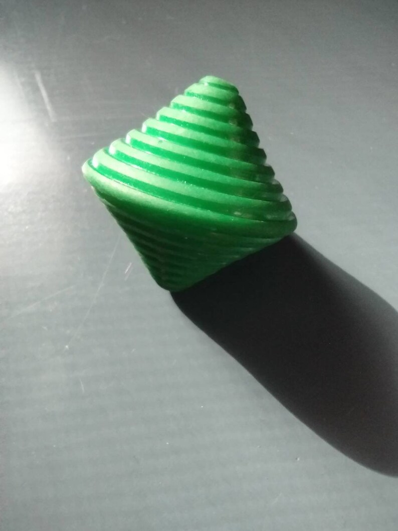 May include: A green plastic spinning top with a spiral design. The top is made of multiple layers of plastic that are stacked on top of each other.
