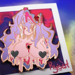 May include: A pin featuring a stylized anime character with pink skin, purple hair, and a gold outline. The character has black heart-shaped coverings over the chest. The pin is on a white card with the artist's signature in the bottom right corner.