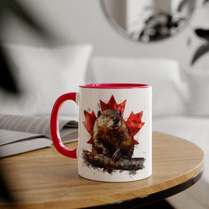 May include: A white ceramic mug with a red handle and rim. The mug displays a watercolour illustration of a groundhog, set against a red maple leaf, a Canadian symbol. Ideal for a Canadian or anyone who loves groundhogs.