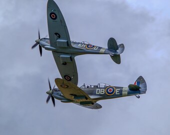 May include: Two vintage, gray and blue, single-engine propeller airplanes flying in formation. The top plane is labeled "KHOU" and the bottom plane is labeled "DBOE".