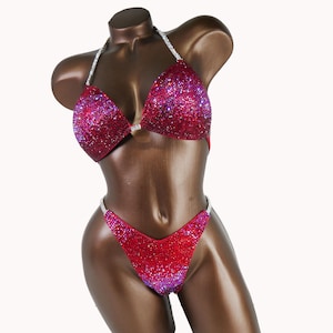 May include: A red and purple sequined bikini with silver straps. The bikini top has a V-neck and the bottom has a high-cut leg.