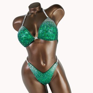 May include: A green and silver sequined bikini competition suit. The suit has a halter top and a v-shaped bottom.