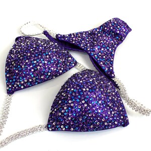 May include: Purple and silver sequined bikini top with a halter strap and a matching bottom. The bikini is decorated with rhinestones.