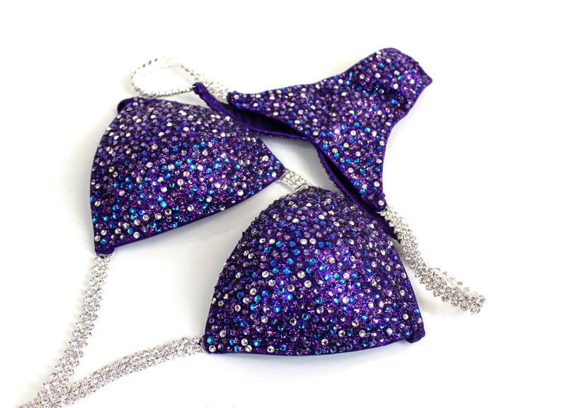 May include: Purple and silver sequined bikini top with a halter strap and a matching bottom. The bikini is decorated with rhinestones.
