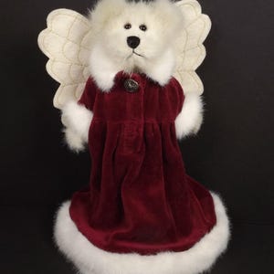 Puede incluir: Un oso de peluche blanco vestido de &aacute;ngel. El oso lleva un vestido de terciopelo burdeos con ribete de piel sint&eacute;tica blanca y un bot&oacute;n decorativo. Tiene alas color crema y un cuello de piel blanca.