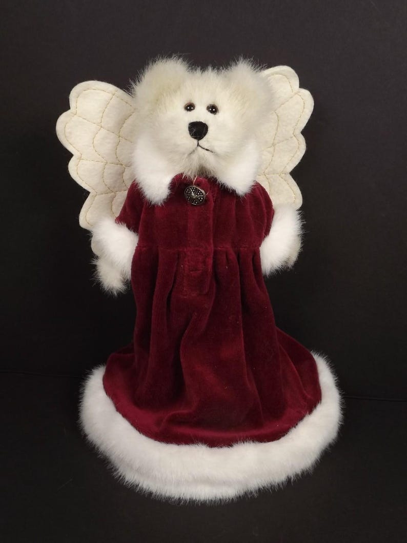 Puede incluir: Un oso de peluche blanco vestido de &aacute;ngel. El oso lleva un vestido de terciopelo burdeos con ribete de piel sint&eacute;tica blanca y un bot&oacute;n decorativo. Tiene alas color crema y un cuello de piel blanca.