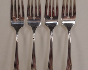 May include: Four silver forks with ornate floral designs on the handles. The forks are arranged in a row, with the tines facing up.