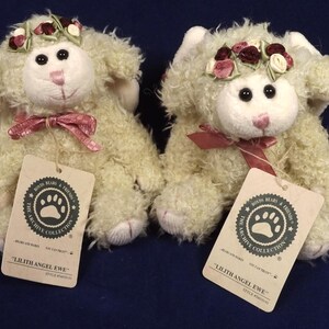 Puede incluir: Dos ovejas de peluche color crema, cada una con una corona floral y un lazo rosa. Los juguetes tienen ojos negros y narices rosas. Cada uno tiene una etiqueta que dice "Lilith Angel Ewe".