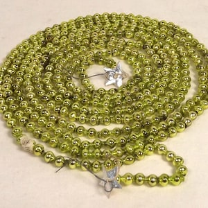 May include: A long strand of lime green metallic beads arranged in a circular coil. The string of beads features small, silver-colored star-shaped accents interspersed throughout the length of the garland, creating a reflective and decorative effect.