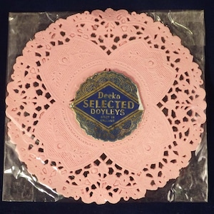 May include: A pink paper doily with a blue and gold label that reads "Deeka Selected Doyleys Made in England".