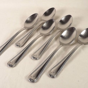 May include: Six silver spoons with ornate handles. The spoons are arranged in a row, with the handles pointing in different directions.