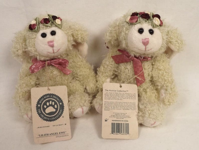 Puede incluir: Dos ovejas de peluche con pelo rizado color crema. Cada una tiene una cara blanca, ojos negros y nariz y boca rosas. Llevan una corona floral y un lazo de cinta rosa. Las etiquetas dicen "Lilith Angel Ewe" y "The Archive Collection."