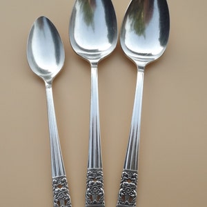 Pode incluir: Três colheres de prata de tamanhos diferentes com desenhos ornamentados nas alças.