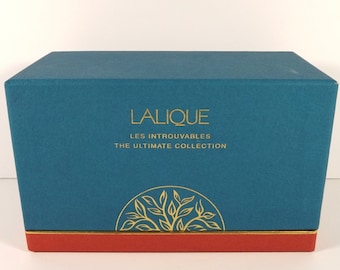 May include: A teal blue box with gold lettering that reads "Lalique Les Introuvables The Ultimate Collection". The box has a gold and red trim and a gold tree design on the front.