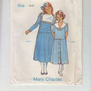 Könnte beinhalten: Ein Vintage-Schnittmuster für ein Mädchenkleid. Das Schnittmuster ist für die Größen 10-12 und bietet zwei verschiedene Kleidstyles. Der erste Style ist ein langärmliges Kleid mit Peter-Pan-Kragen und einem gerafften Rock. Der zweite Style ist ein kurzärmeliges Kleid mit einer Schleife am Ausschnitt und einer Knopfleiste vorne. Das Schnittmuster ist von Mary Charles.