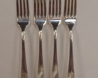 May include: Four silver forks with tines and floral design on the handles. The forks are arranged in a row against a neutral background. The tines are sharp and the handles have a decorative floral pattern near the base.