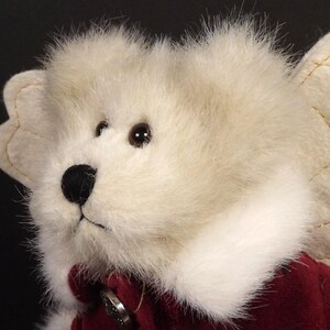 Puede incluir: Primer plano de un oso de peluche &aacute;ngel con pelaje color crema y un atuendo de terciopelo rojo. El oso tiene una nariz negra, ojos marrones y un cuello blanco. Las alas de &aacute;ngel son de color crema con costuras doradas.