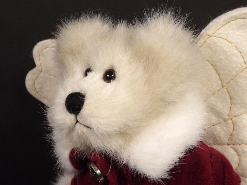 Puede incluir: Primer plano de un oso de peluche &aacute;ngel con pelaje color crema y un atuendo de terciopelo rojo. El oso tiene una nariz negra, ojos marrones y un cuello blanco. Las alas de &aacute;ngel son de color crema con costuras doradas.