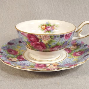 May include: A floral teacup and saucer set with a blue and white background and pink roses. The cup and saucer have a gold trim.