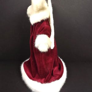 Puede incluir: Un disfraz de Pap&aacute; Noel de terciopelo burdeos con ribete de piel sint&eacute;tica blanca. El disfraz incluye un gorro, pu&ntilde;os y un abrigo largo. El ribete blanco est&aacute; alrededor del gorro, los pu&ntilde;os y la parte inferior del abrigo.