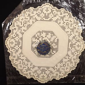 May include: A white paper doily with a delicate lace pattern. The doily is packaged in a clear plastic bag with a blue and gold label that reads "Doily - Selected Doilies".