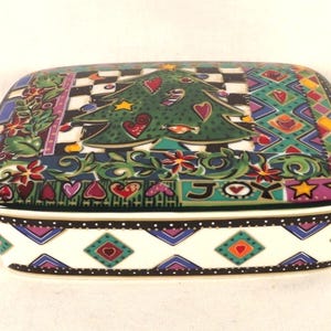 Puede incluir: Una caja de cerámica con un diseño de árbol de Navidad colorido. La tapa presenta un árbol verde con corazones rojos, bastones de caramelo y estrellas. La caja tiene un fondo blanco con un patrón geométrico negro, verde y azul.