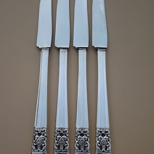 Pode incluir: Quatro facas de jantar de prata com desenhos florais ornamentados nas alças.