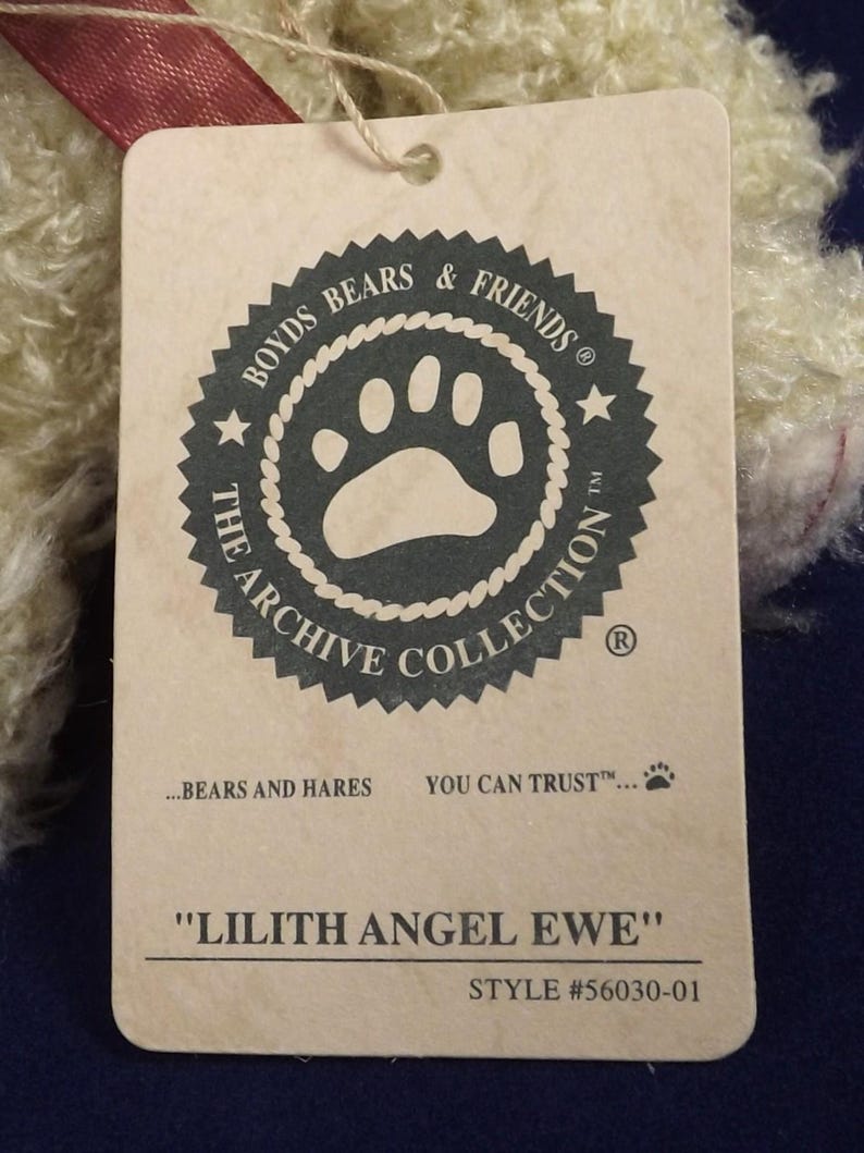 Puede incluir: Una etiqueta crema con el texto "BOYDS BEARS & FRIENDS" y "THE ARCHIVE COLLECTION". La etiqueta tambi&eacute;n dice "LILITH ANGEL EWE" y "STYLE #56030-01". Una cinta roja est&aacute; unida a la etiqueta.