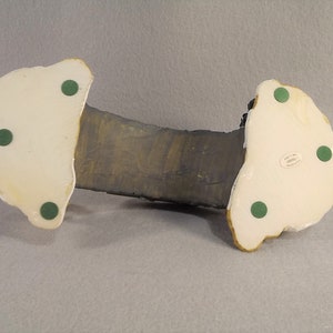 May include: A ceramic figurine of a black cat with green eyes, sitting on a rock. The figurine has a white base with four green felt pads on the bottom.