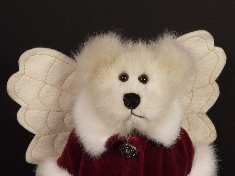 Puede incluir: Un oso de peluche blanco con alas de &aacute;ngel color crema. El oso tiene una nariz negra y ojos marrones. Lleva un abrigo de terciopelo burdeos con un bot&oacute;n decorativo. Las alas est&aacute;n cosidas con hilo dorado.