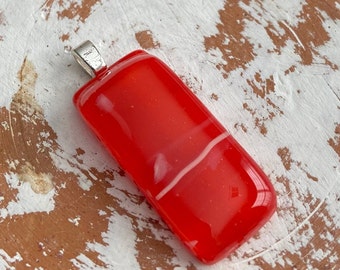 May include: A rectangular red pendant with a white stripe across the middle. The pendant has a silver-colored bail at the top for attaching to a chain. The pendant is made of glass.