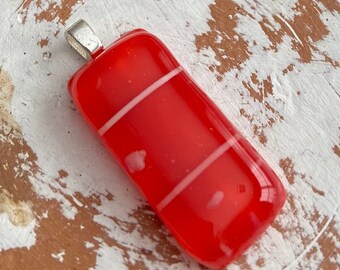 May include: A rectangular red glass pendant with two white stripes. The pendant has a silver-colored bail for attaching to a chain. The glass is glossy and has a slight curve.