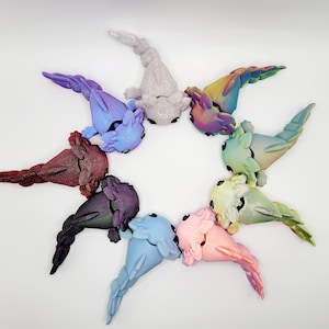 May include: A collection of nine axolotl figurines, each with a different color and iridescent finish. The axolotls are arranged in a circle, with their tails pointing outwards.