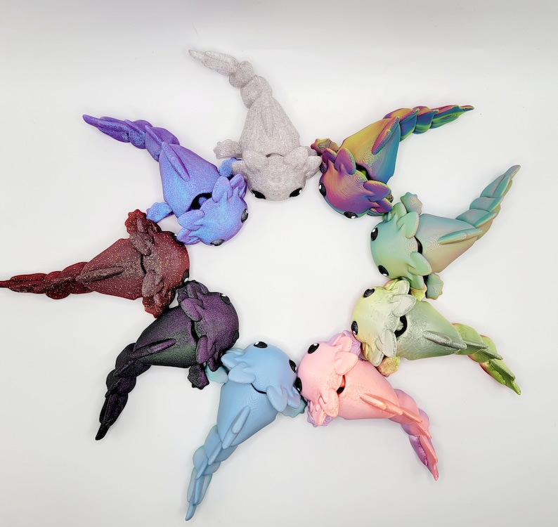 May include: A collection of nine axolotl figurines, each with a different color and iridescent finish. The axolotls are arranged in a circle, with their tails pointing outwards.