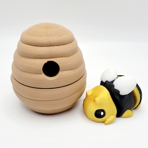 May include: A small, brown, beehive-shaped toy with a round hole in the front. A small, yellow and black bee toy is next to the beehive.