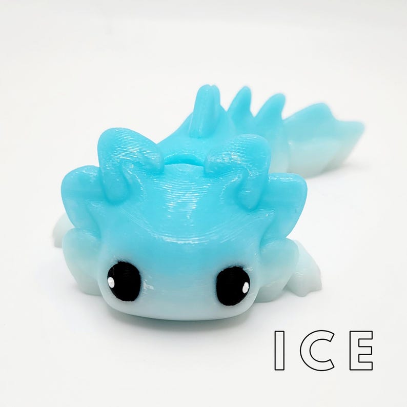 May include: A small, blue and white axolotl figurine with black eyes. The figurine is made of a smooth, glossy material and has a gradient color scheme. The word "ICE" is printed in black letters below the figurine.