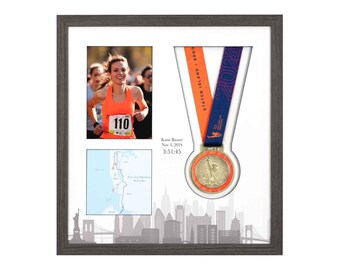 Puede incluir: Enmarcado conmemorativo del Maratón de Nueva York. Incluye una foto de un corredor con el dorsal 110, un mapa de la carrera y una medalla de finalista. La medalla es dorada con una cinta naranja y azul. El marco es gris.