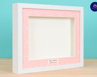 May include: White shadow box frame with a pink floral patterned mat. The frame has a label that reads "Clara Miller, 18th May 2023".