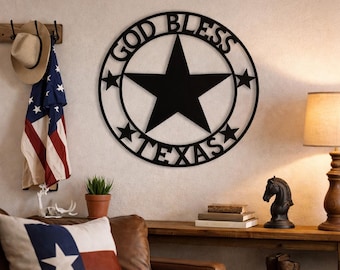 May include: Black metal wall art with the words "GOD BLESS TEXAS" encircling a large star. The art is displayed on a white wall, with a cowboy hat and American flag hanging nearby. A decorative pillow with a star design is also visible.