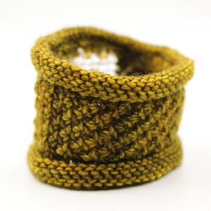K&ouml;nnte beinhalten: Ein handgestrickter Korb in Senfgelb. Der zylindrische Korb hat einen ausgestellten Boden und einen gerollten oberen Rand. Das strukturierte Strickmuster verleiht ihm ein dichtes, robustes Aussehen. Die warme, erdige Farbe eignet sich f&uuml;r verschiedene Einrichtungsstile. Der Korb ist ca. 10 cm hoch.