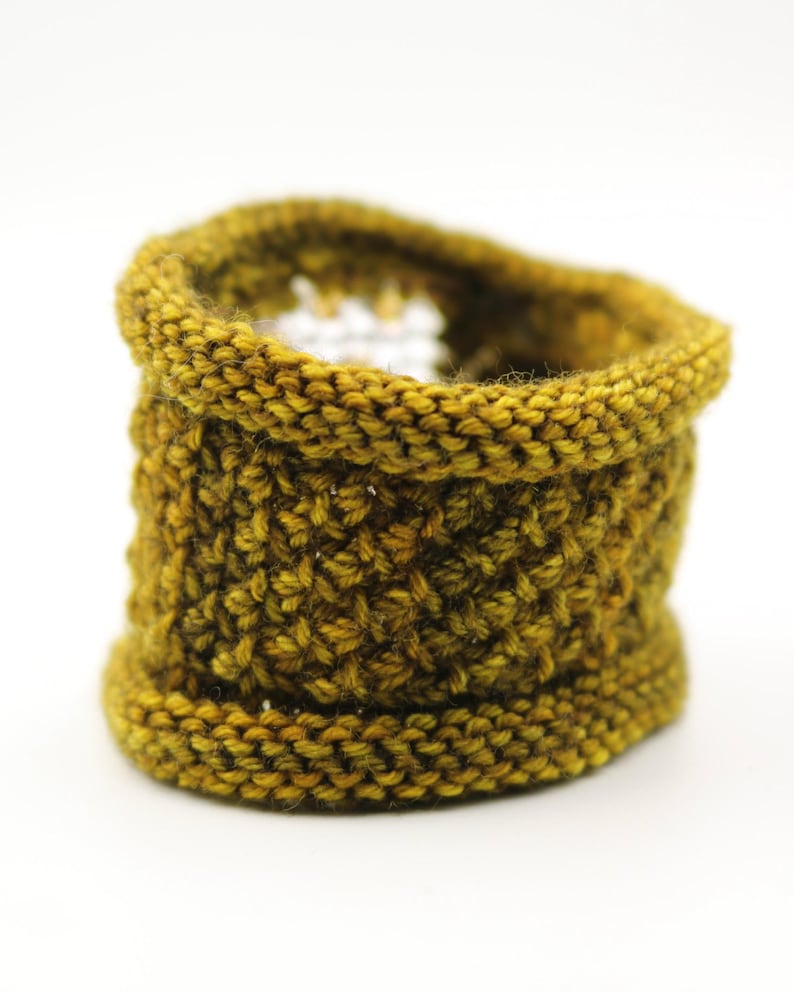 K&ouml;nnte beinhalten: Ein handgestrickter Korb in Senfgelb. Der zylindrische Korb hat einen ausgestellten Boden und einen gerollten oberen Rand. Das strukturierte Strickmuster verleiht ihm ein dichtes, robustes Aussehen. Die warme, erdige Farbe eignet sich f&uuml;r verschiedene Einrichtungsstile. Der Korb ist ca. 10 cm hoch.
