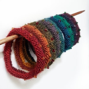 May include: A set of seven knitted bracelets in a rainbow of colors, each with a row of sparkling jewel-toned beads.