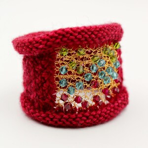 K&ouml;nnte beinhalten: Ein gestricktes rotes Armband mit einem goldenen Mesh-Overlay. Das Mesh ist mit farbigen Perlen in Rot-, Gr&uuml;n- und Blaut&ouml;nen verziert. Ein einzigartiges handgefertigtes Accessoire.