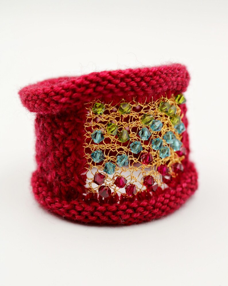 K&ouml;nnte beinhalten: Ein gestricktes rotes Armband mit einem goldenen Mesh-Overlay. Das Mesh ist mit farbigen Perlen in Rot-, Gr&uuml;n- und Blaut&ouml;nen verziert. Ein einzigartiges handgefertigtes Accessoire.