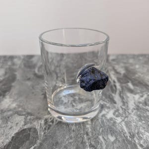 May include: A clear glass shot glass with a dark blue rock attached to the rim.