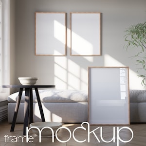 May include: Three wooden picture frames with white mats, two are hanging on a light gray wall and one is on the floor next to a light gray couch. The frames are empty and ready for your photos or artwork.