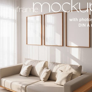 Puede incluir: Dos imágenes enmarcadas con paspartús blancos y marcos de madera colgadas en una pared blanca sobre un sofá beige con almohadas. El texto "frame mockup with photoshop DIN A ratio" es visible en la esquina superior derecha de la imagen.