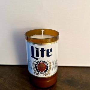 May include: A white candle in a clear glass bottle with a brown label that says "Lite" and "A Fine Pilsner Beer".