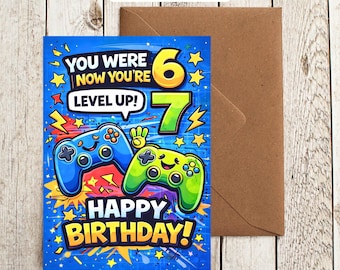 May include: A rectangular birthday greeting card featuring a blue background with yellow stars and lightning bolts. It displays two cartoon game controllers, one blue and one green, with the text: YOU WERE 6 NOW YOU'RE 7 LEVEL UP! HAPPY BIRTHDAY!