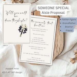 May include: Two white cards with black text. One card reads "Will you walk me down the Aisle?" with a floral accent. The other card reads "the moments that built me." The cards are part of a wedding proposal set.